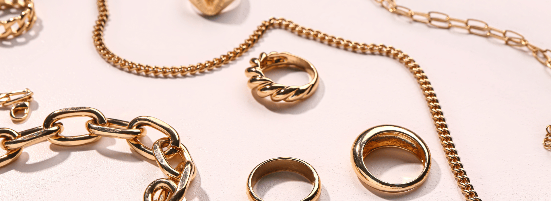 תכשיטים בסיטונאות: טבעות, עגילים וצמידים בזהב, משתלבים יחד על רקע בהיר.