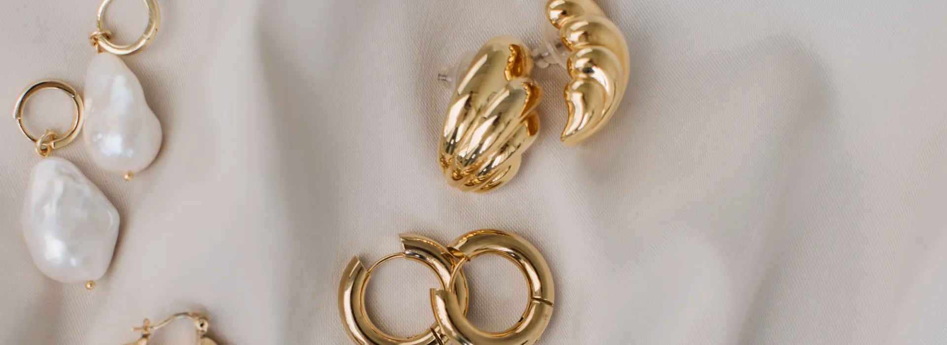 עגילים מעוצבים מזהב עם פנינים, מונחים על בד בהיר, מתאימים לסיטונאות תכשיטים.