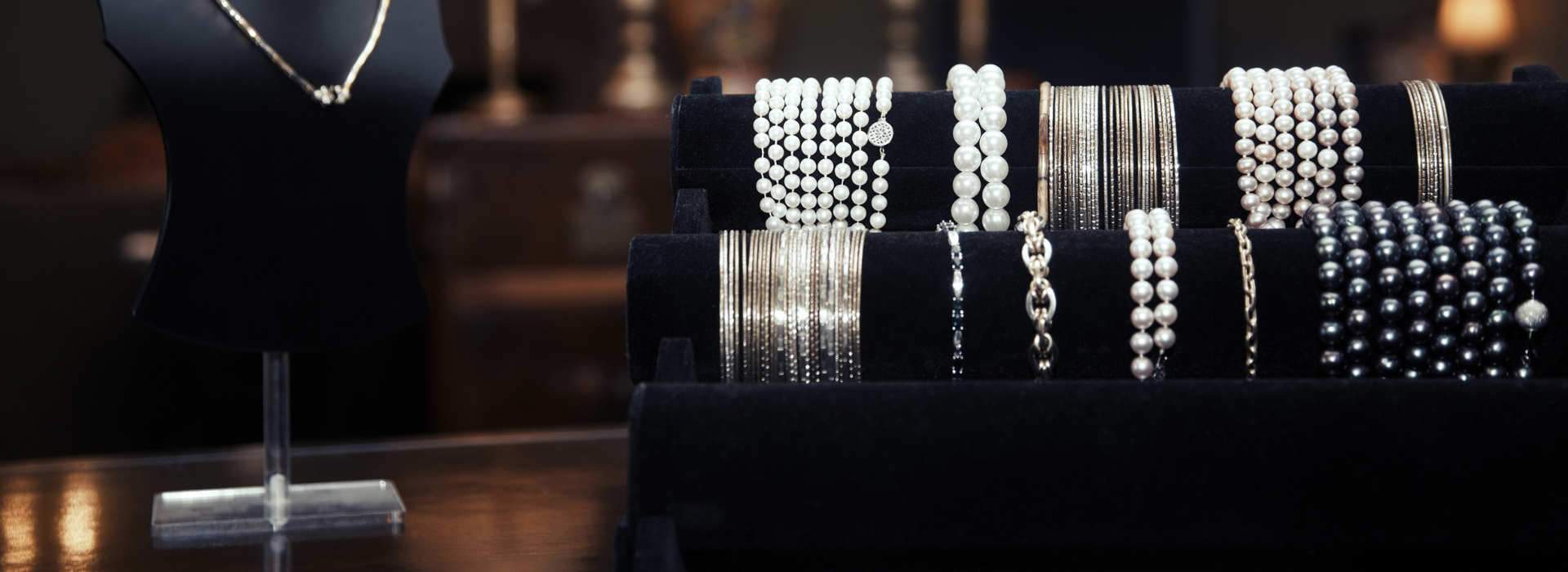 תצוגת תכשיטים בסיטונאות: עגילים, צמידים וטבעות כסף עדינות על רקע כהה.